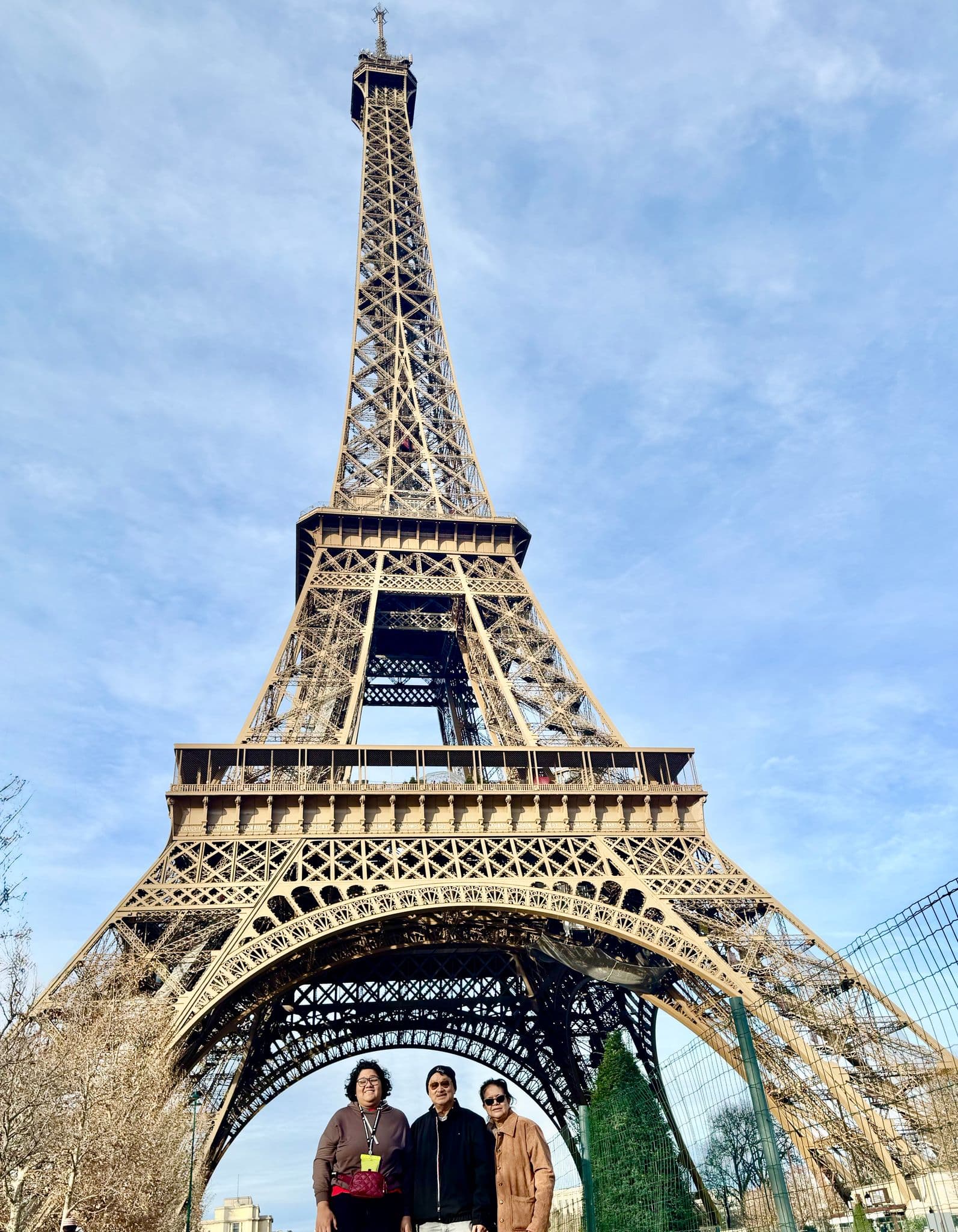 Eiffel Tower towering above three people posing beneath it in Paris, France.