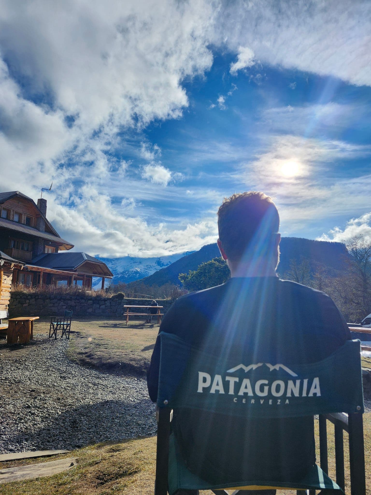 Sunlit Andes mountains in Patagonia with a person seated in a chair labeled "Patagonia" facing the view under a bright sky.