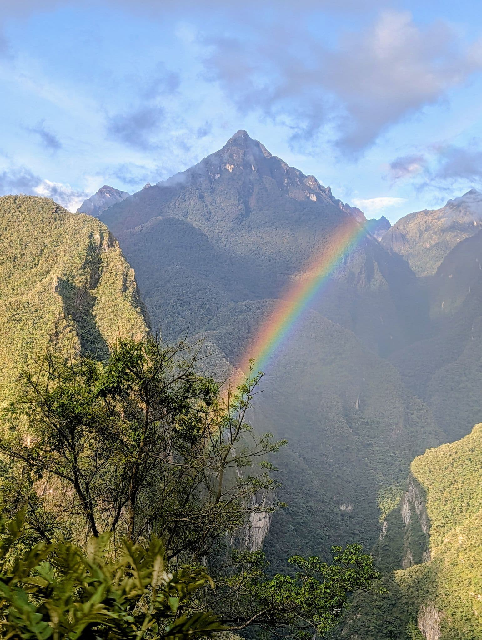 Andean mountain near Machu Picchu, Peru with a vivid rainbow arcing across the valley and trees in the foreground.