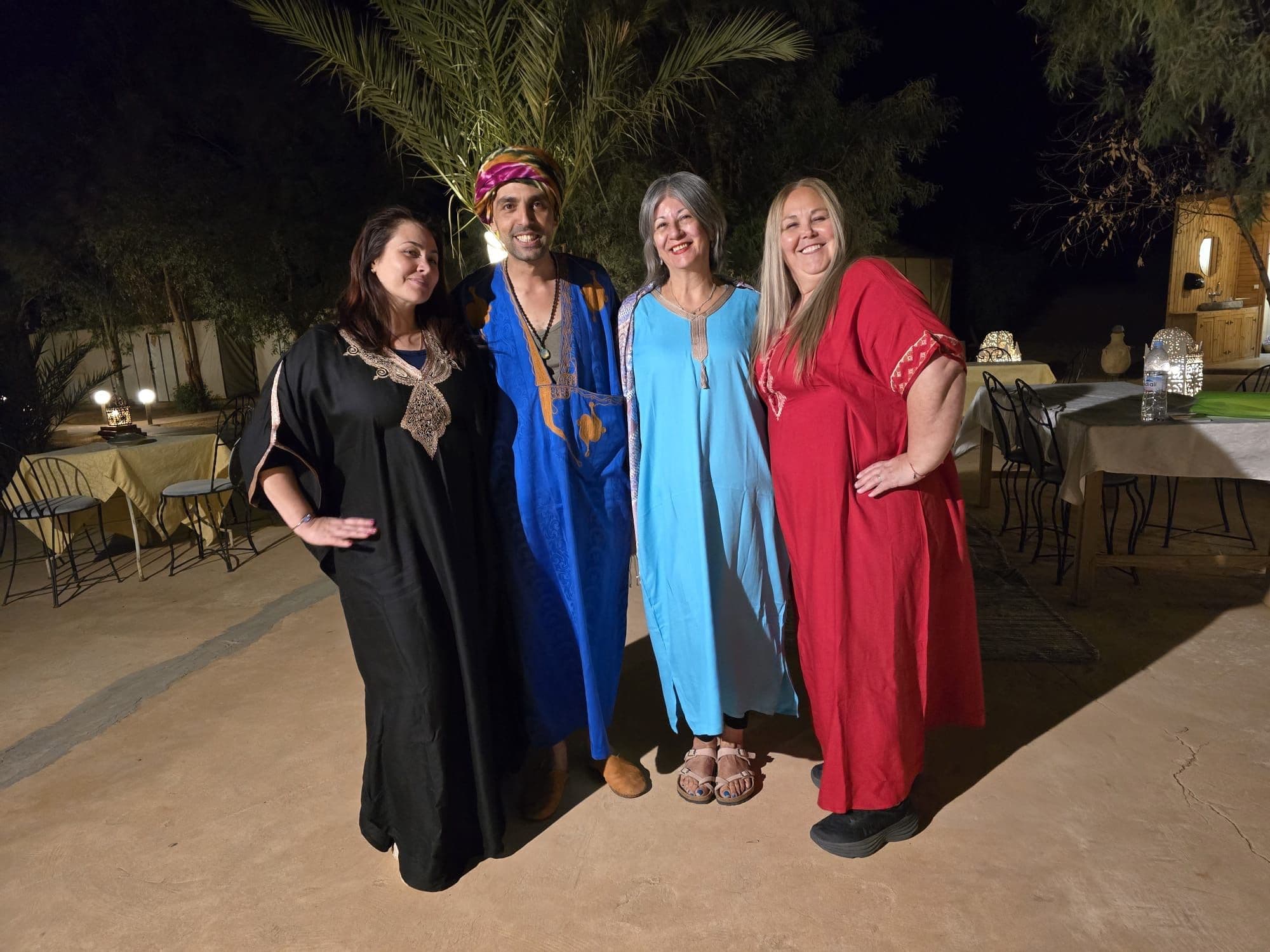 Four travelers in traditional robes posing for a photo at a desert camp in the Sahara Desert, Morocco.