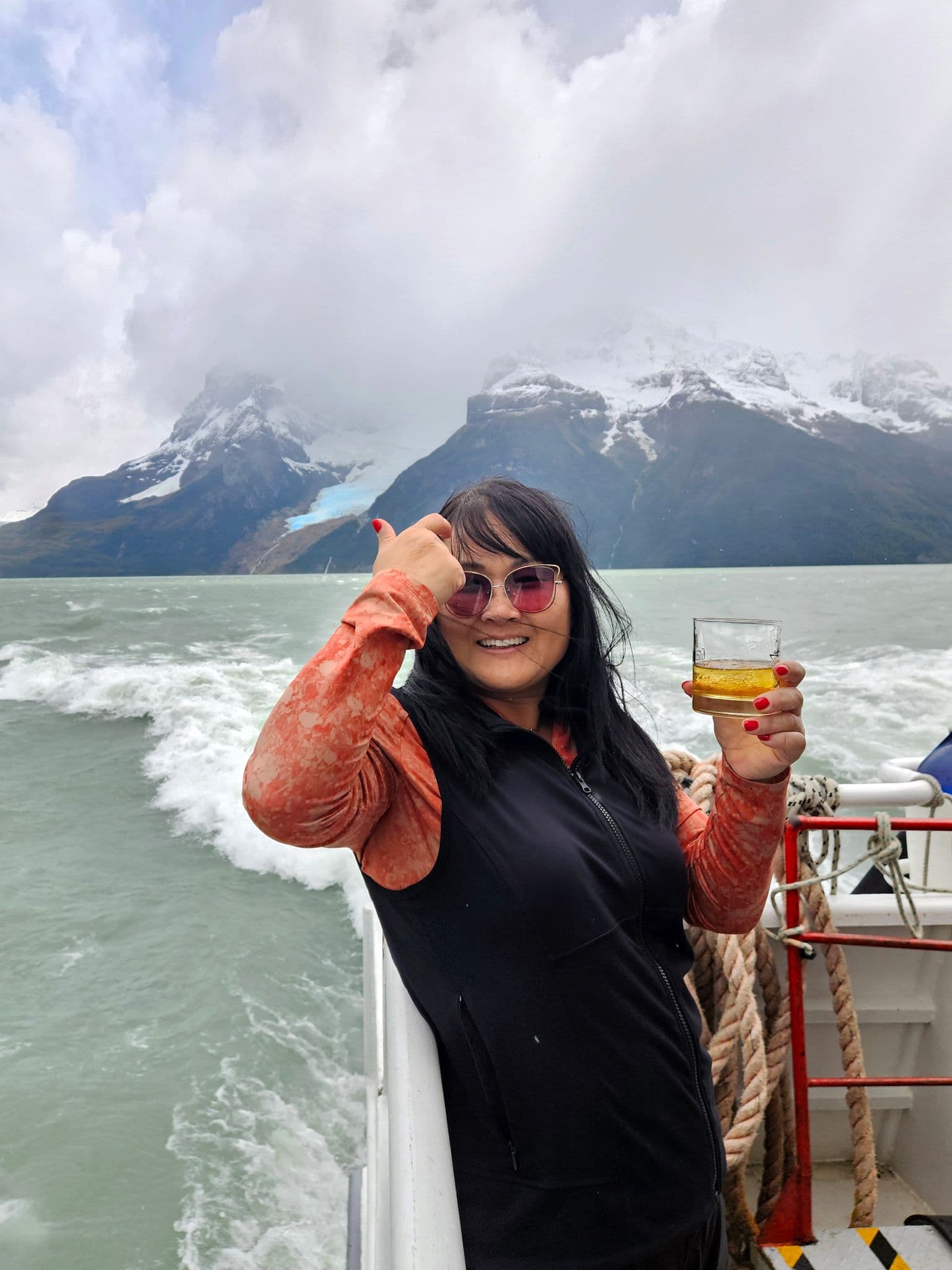 Snow-capped mountains and a glacier in Chilean Patagonia with a woman on a boat holding a glass of whisky.