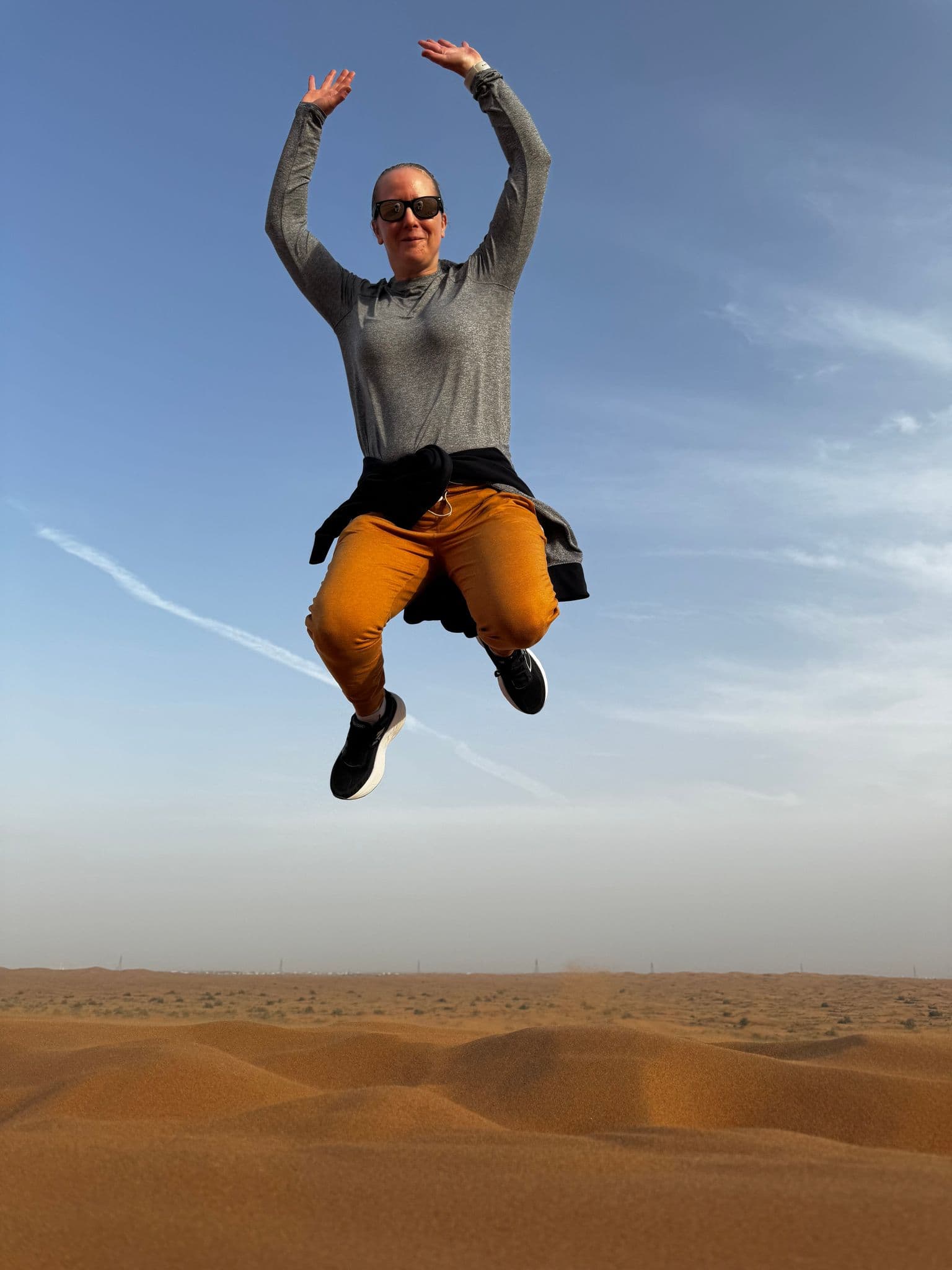 Person jumping above sand dunes during a desert safari tour, United Arab Emirates.