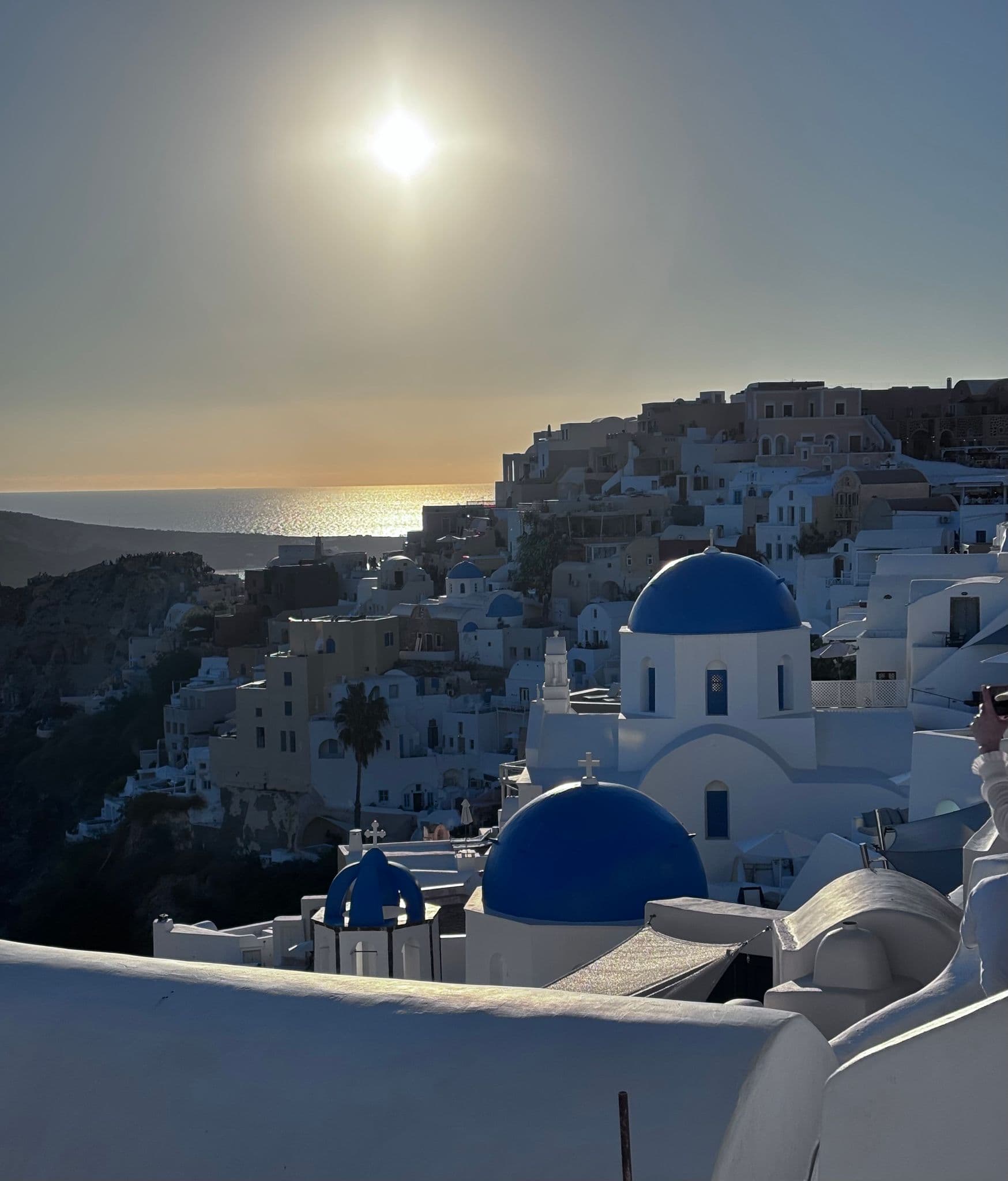Blue-domed churches of Oia on Santorini's cliffside with the sea glowing at sunset, Greece.