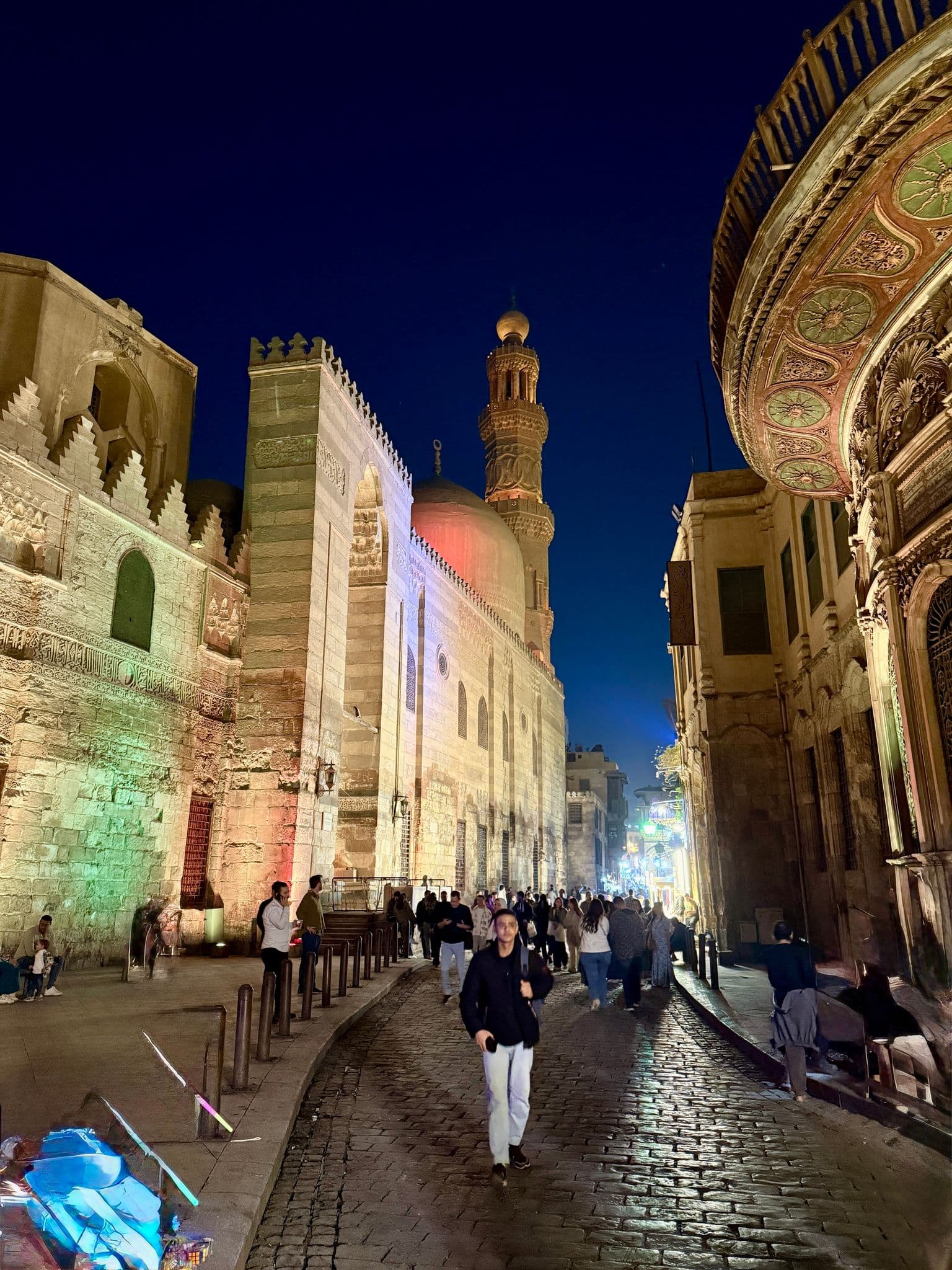 Lit mosque dome and minaret beside Khan el-Khalili street, crowds walking on a cobbled road in Cairo, Egypt