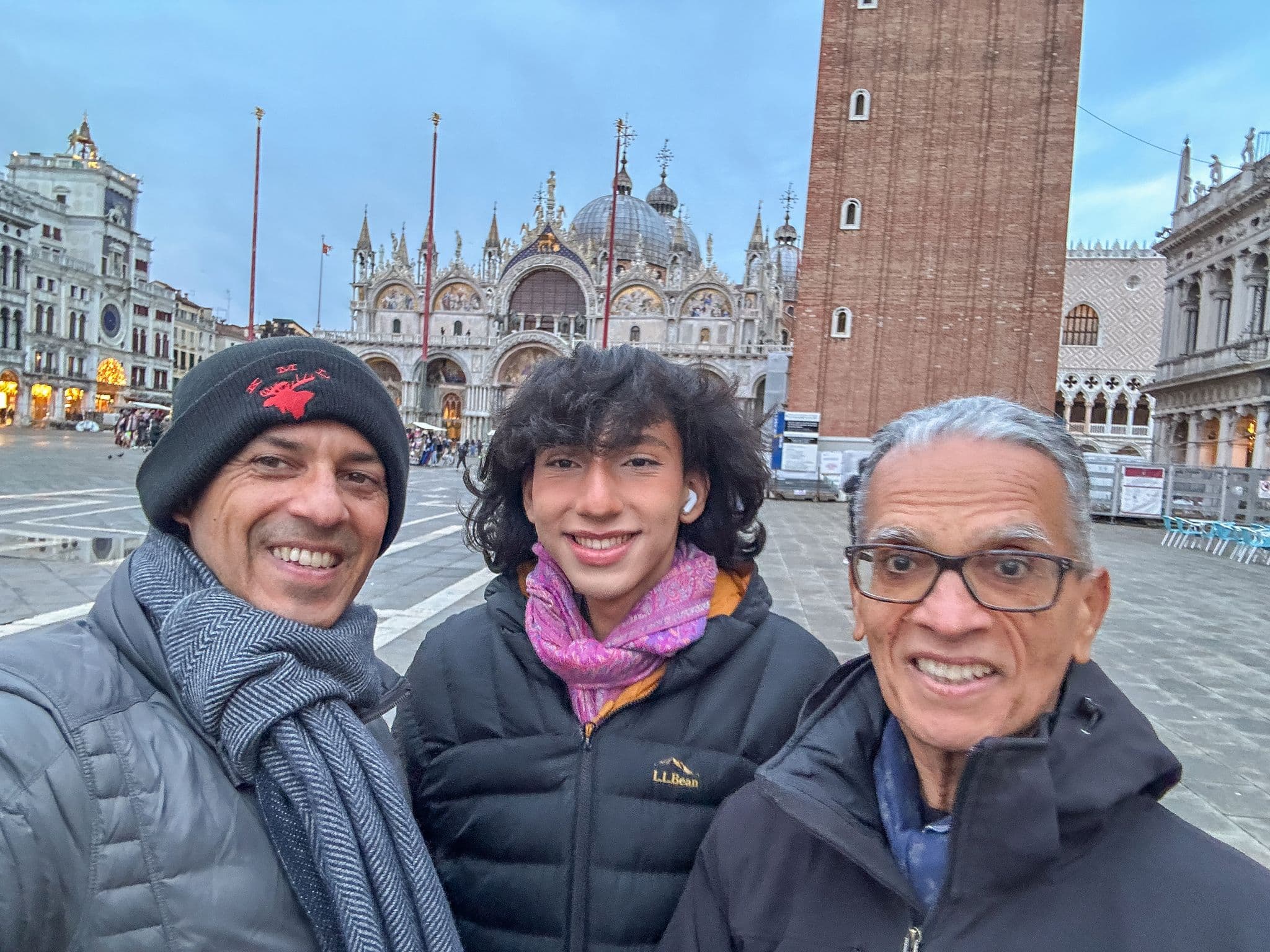 St. Mark's Basilica and Campanile behind three people smiling in a selfie at Piazza San Marco, Venice, Italy.