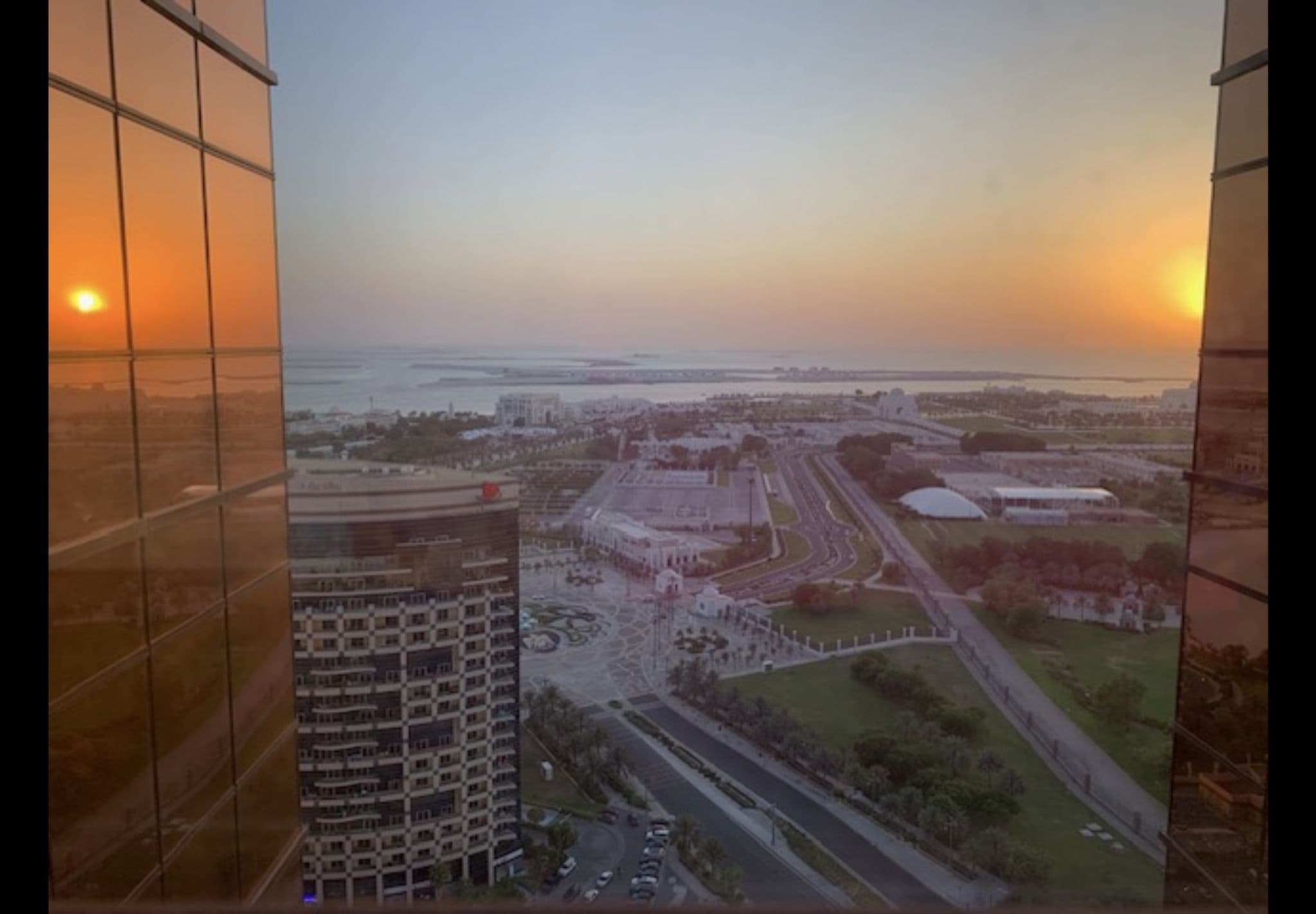 Sunset over a coastal city skyline seen through a high-rise glass window, Abu Dhabi, United Arab Emirates