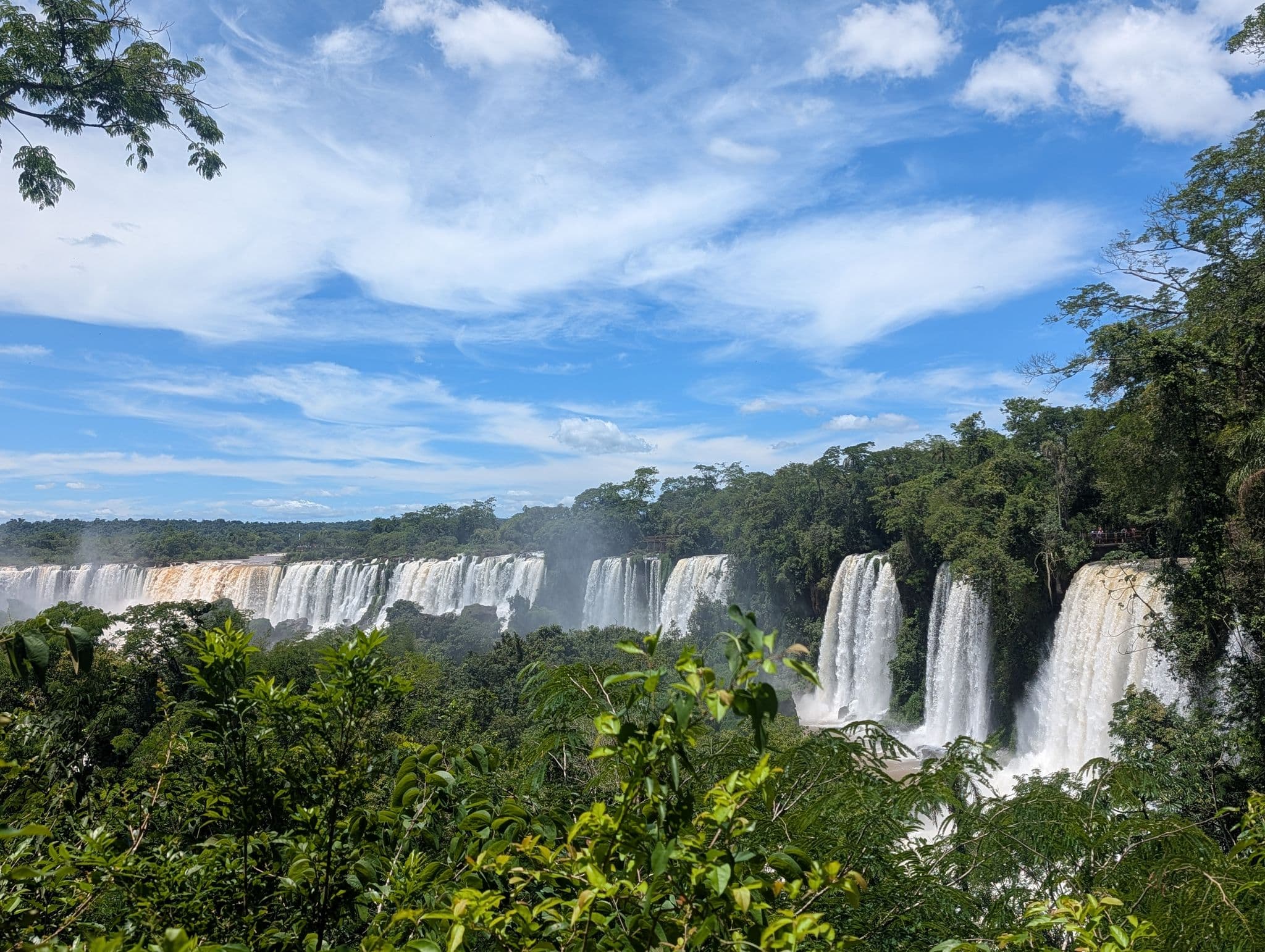 Iguazu Falls cascading over a wide cliffline with rainforest in the foreground and a blue sky, Brazil.