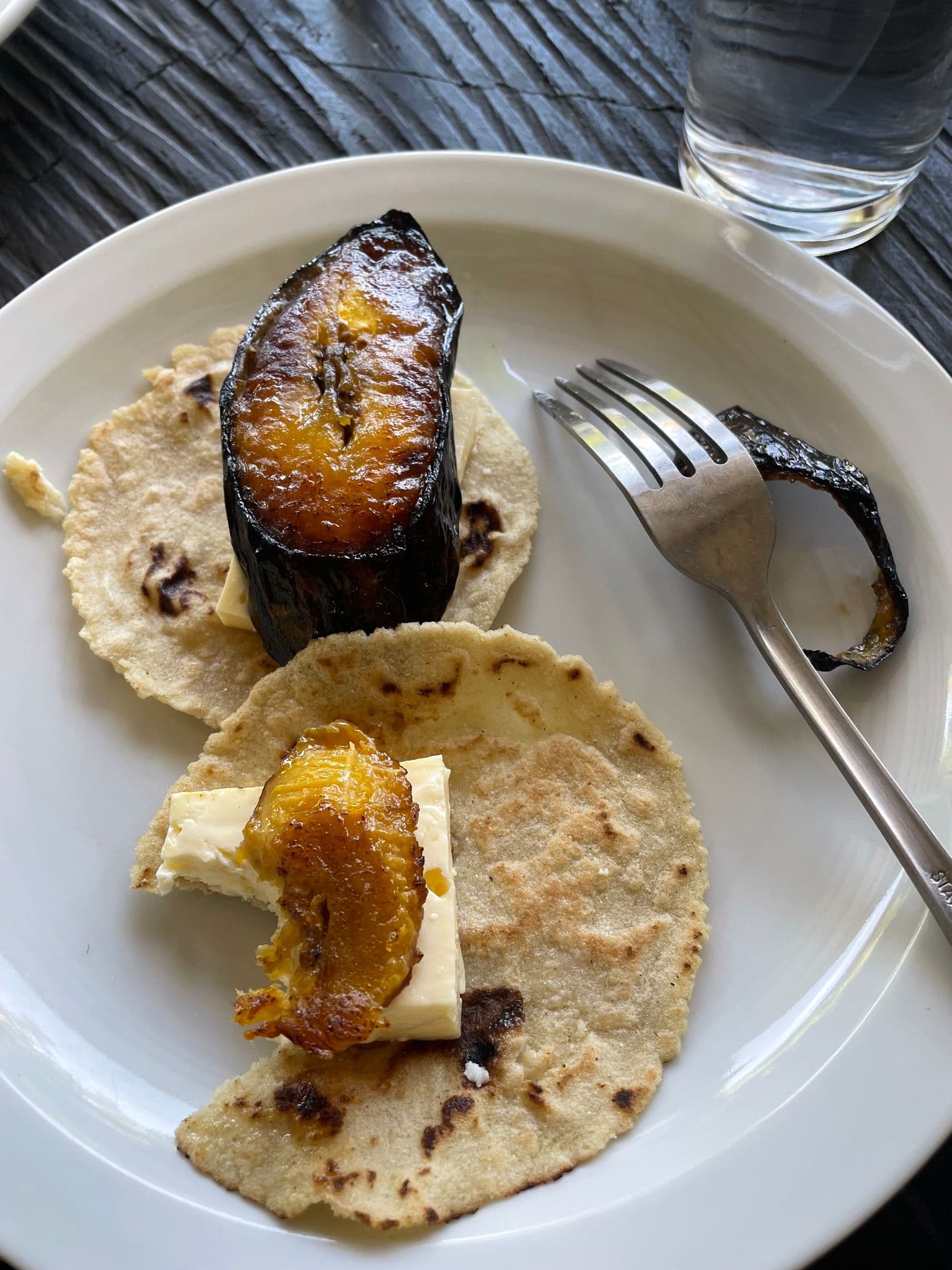 Caramelized plantain and cheese on small corn tortillas on a white plate, table setting in Costa Rica.